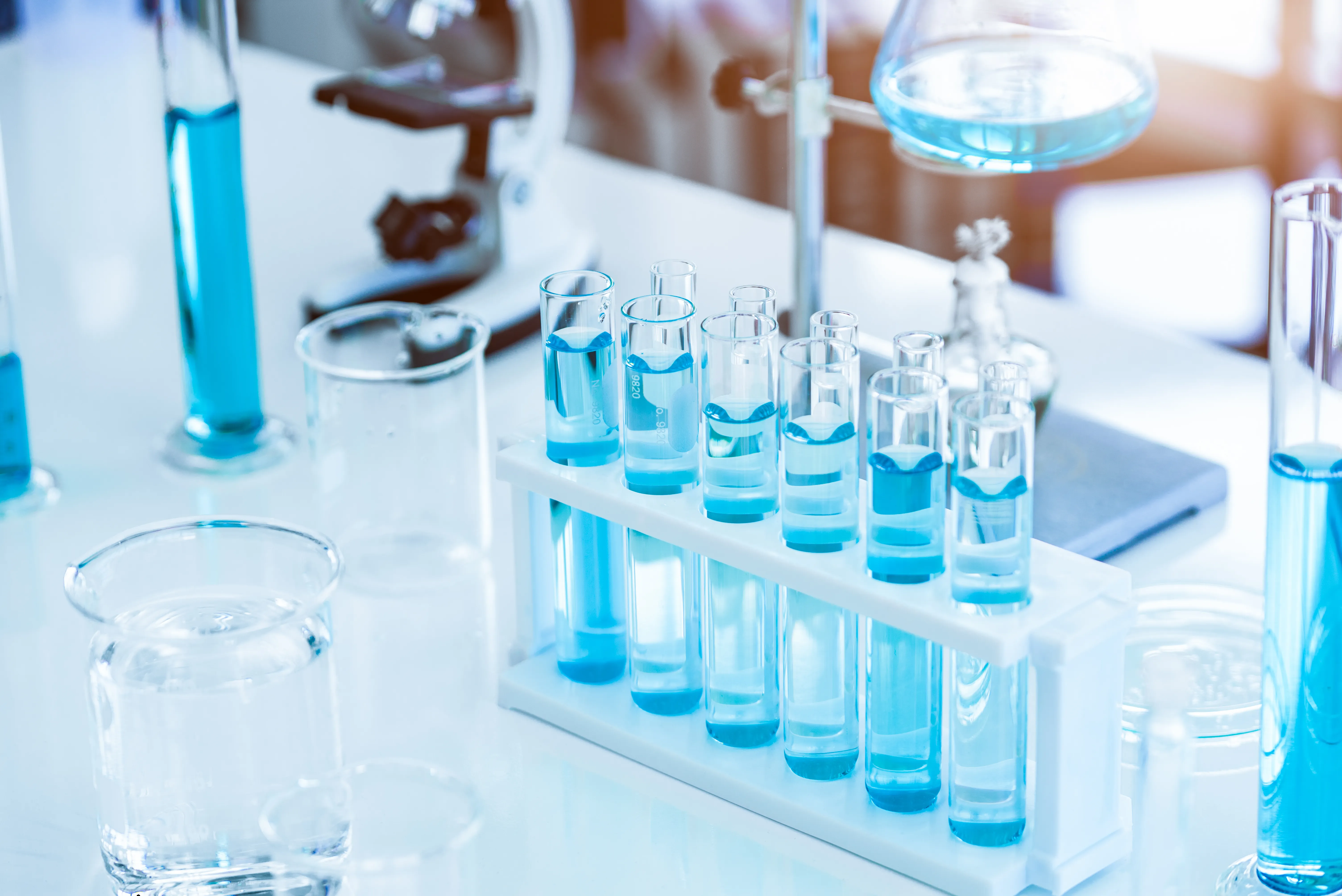 A chemists workbench with beakers, a microscope and test tubes with blue liquid
